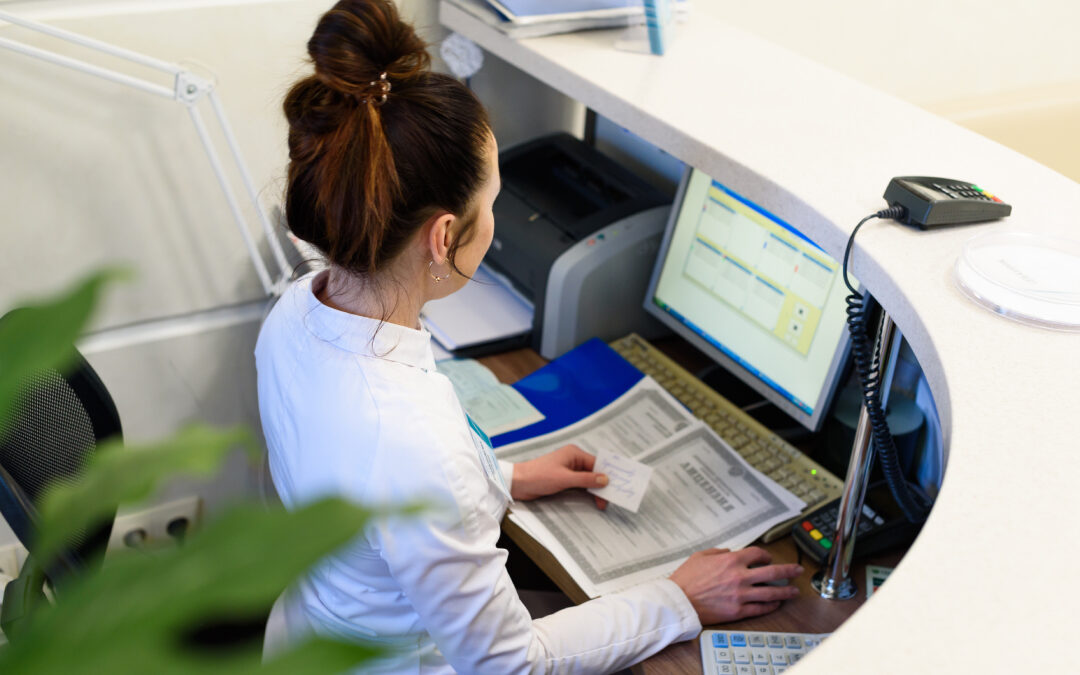 Medical clinic receptionist managing health insurance paperwork and direct billing details on a computer at the front desk.