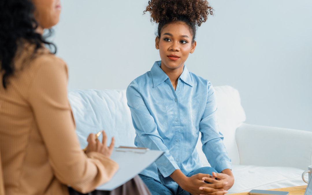 A young woman sitting on a white couch and engaging in a mind-body therapy session with a therapist holding a clipboard at Choice Point Psychological in Calgary.