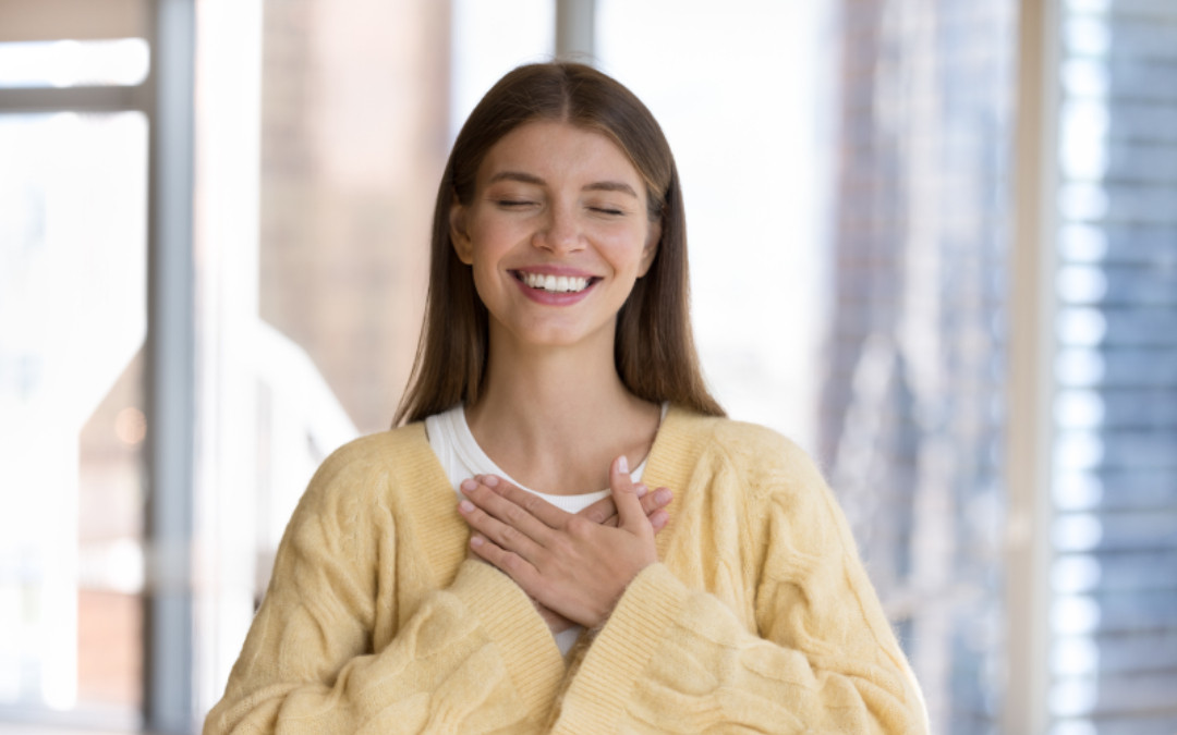 Smiling woman holding both hands over her heart in a gesture of self-compassion, illustrating how EMDR therapy rewrites negative beliefs in Calgary.